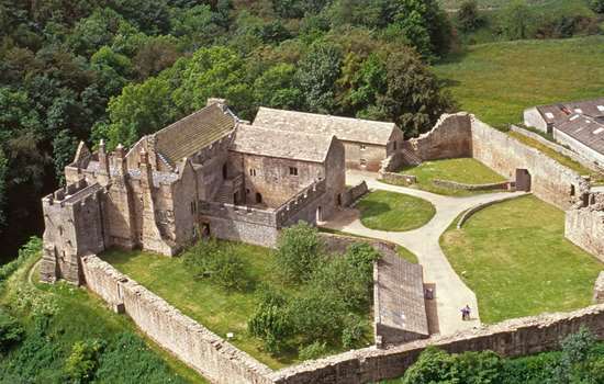 Aerial view of the substantial remains of Aydon Castle perched on the edge of scarp above Cor Burn