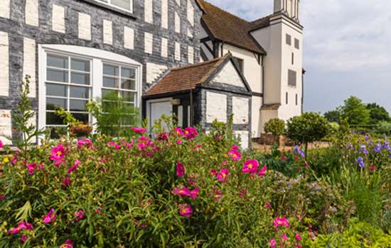 The black and white timber-framed Boscobel House with pink flowers in the garden in the foreground.
