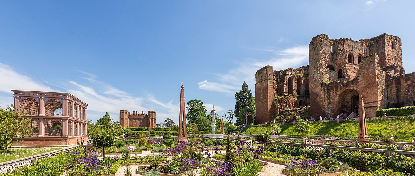The ruins of Kenilworth Castle next to the Elizabethan gardens under a blue sky.