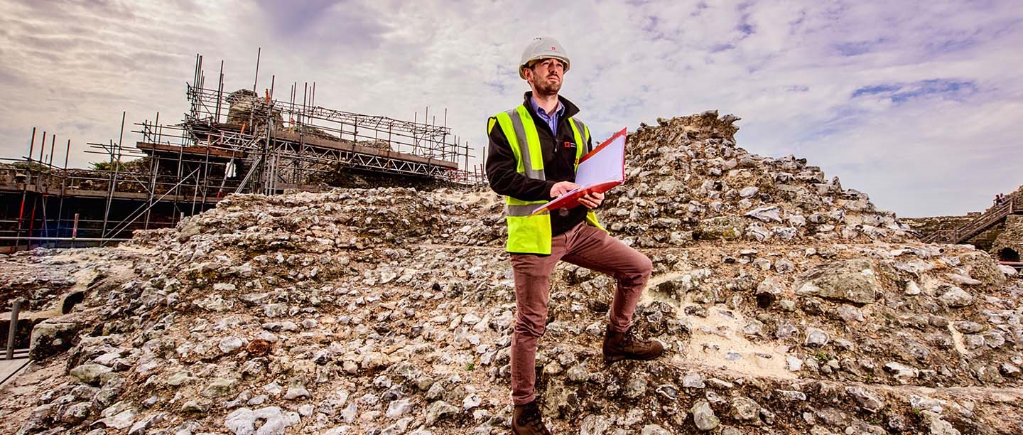 A conservator with a clipboard standing on top of some ruins.