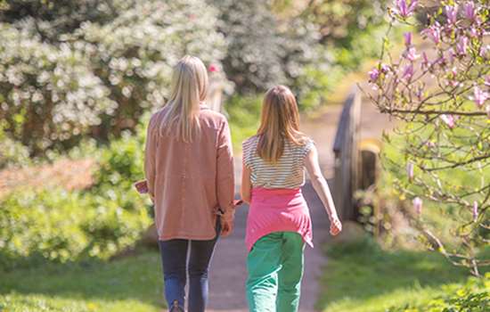 Two women walk away from the camera down a garden path