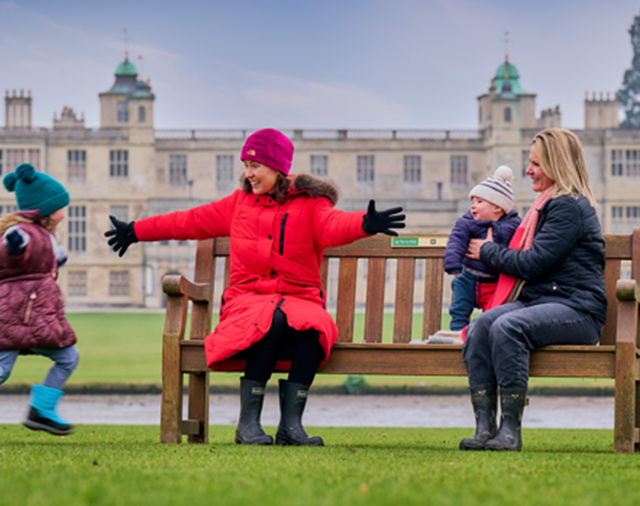 Image: two women are sitting on a bench as a happy child runs towards them 